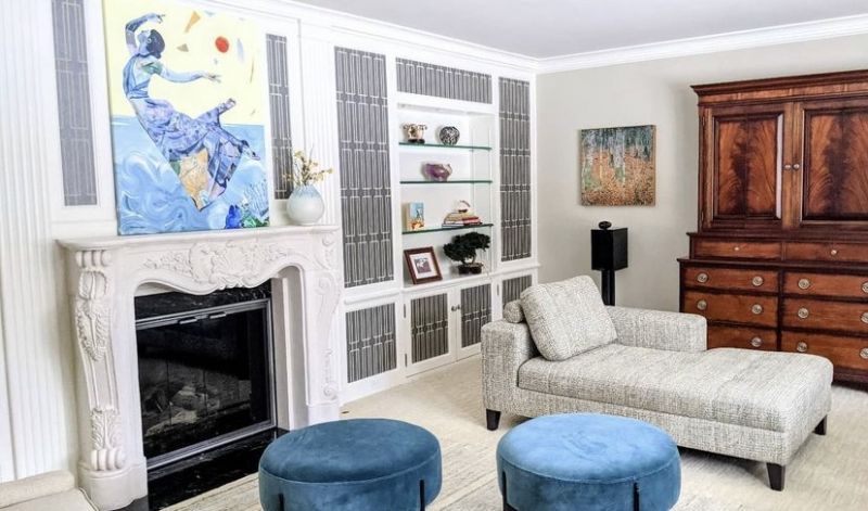 Living room with a carved stone fireplace, built-in shelving, a chaise and blue velvet ottomans