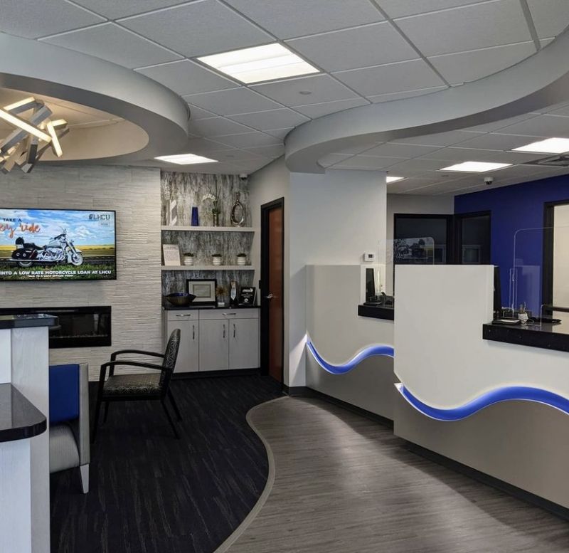 Credit union lobby with curved teller counters lit by blue accent lighting and a stone fireplace wall