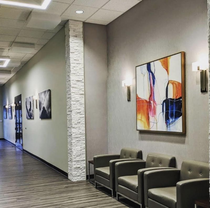 Clinic corridor waiting area with gray leather armchairs, a stacked stone column and framed abstract art